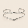 A gold-tone open cuff bangle bracelet with a hammered texture, displayed on a light cream background.
