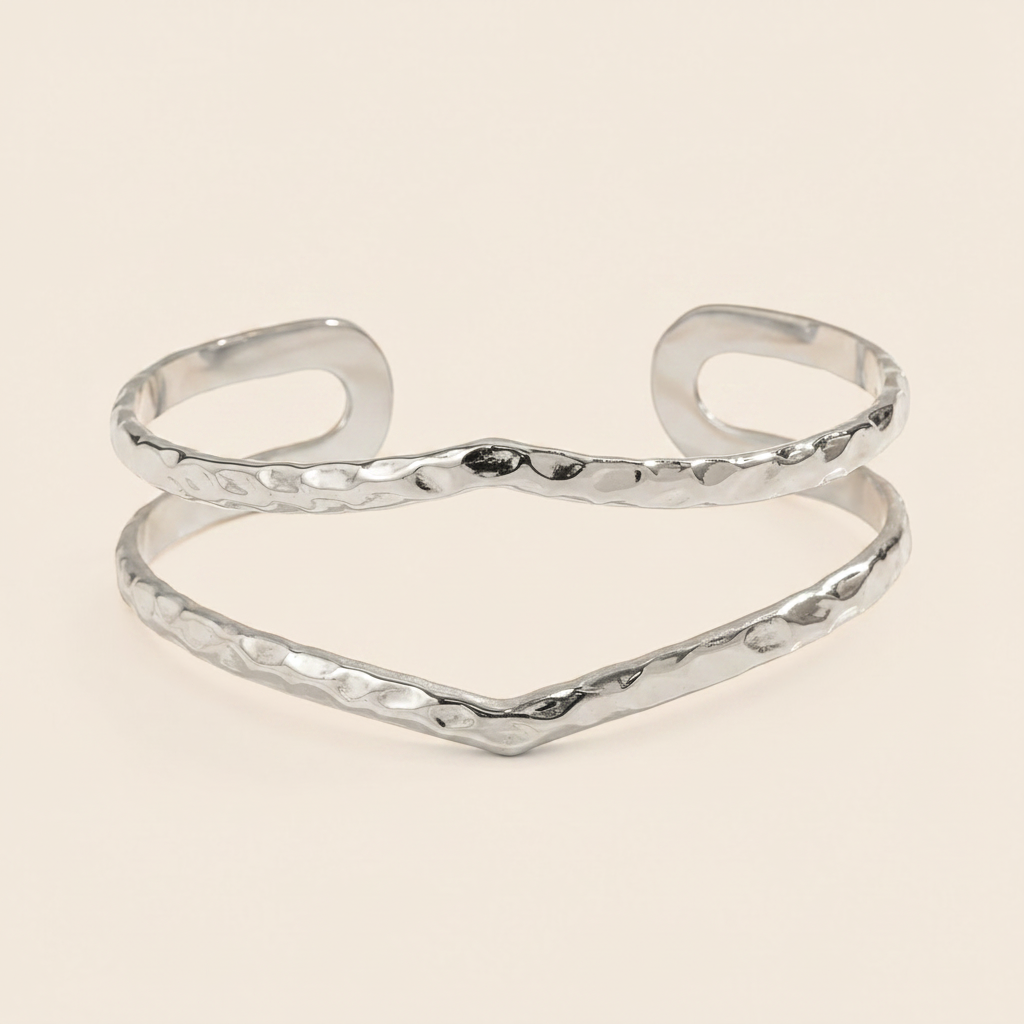 A gold-tone open cuff bangle bracelet with a hammered texture, displayed on a light cream background.