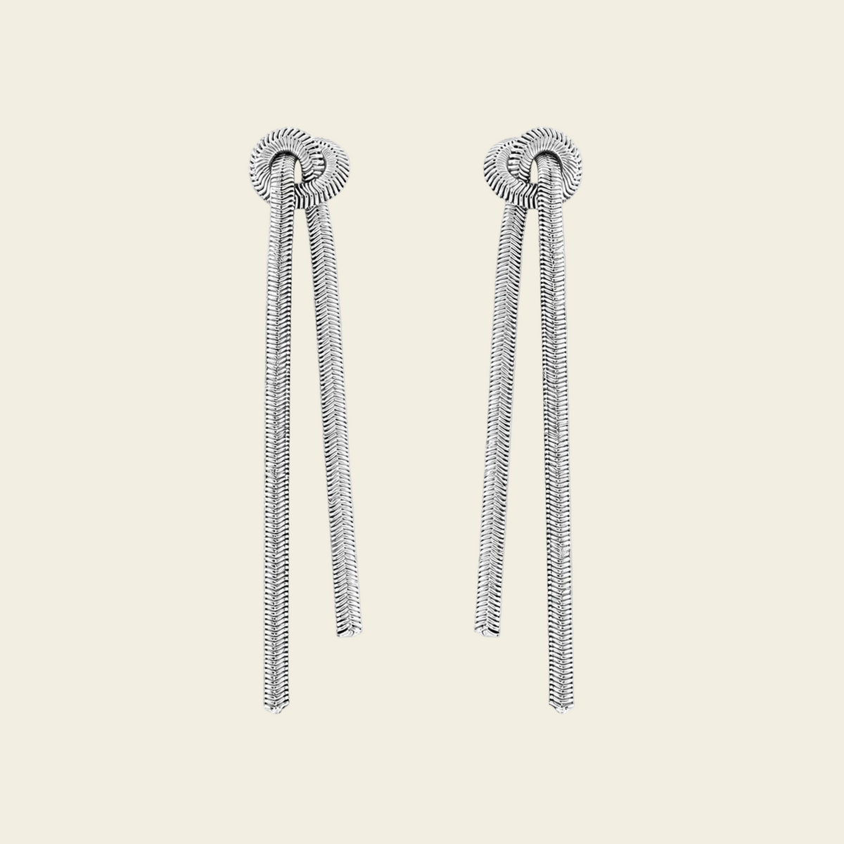 A pair of silver-toned dangle earrings with textured circular studs and long, snake-like draped chains, shown on a plain light beige background.