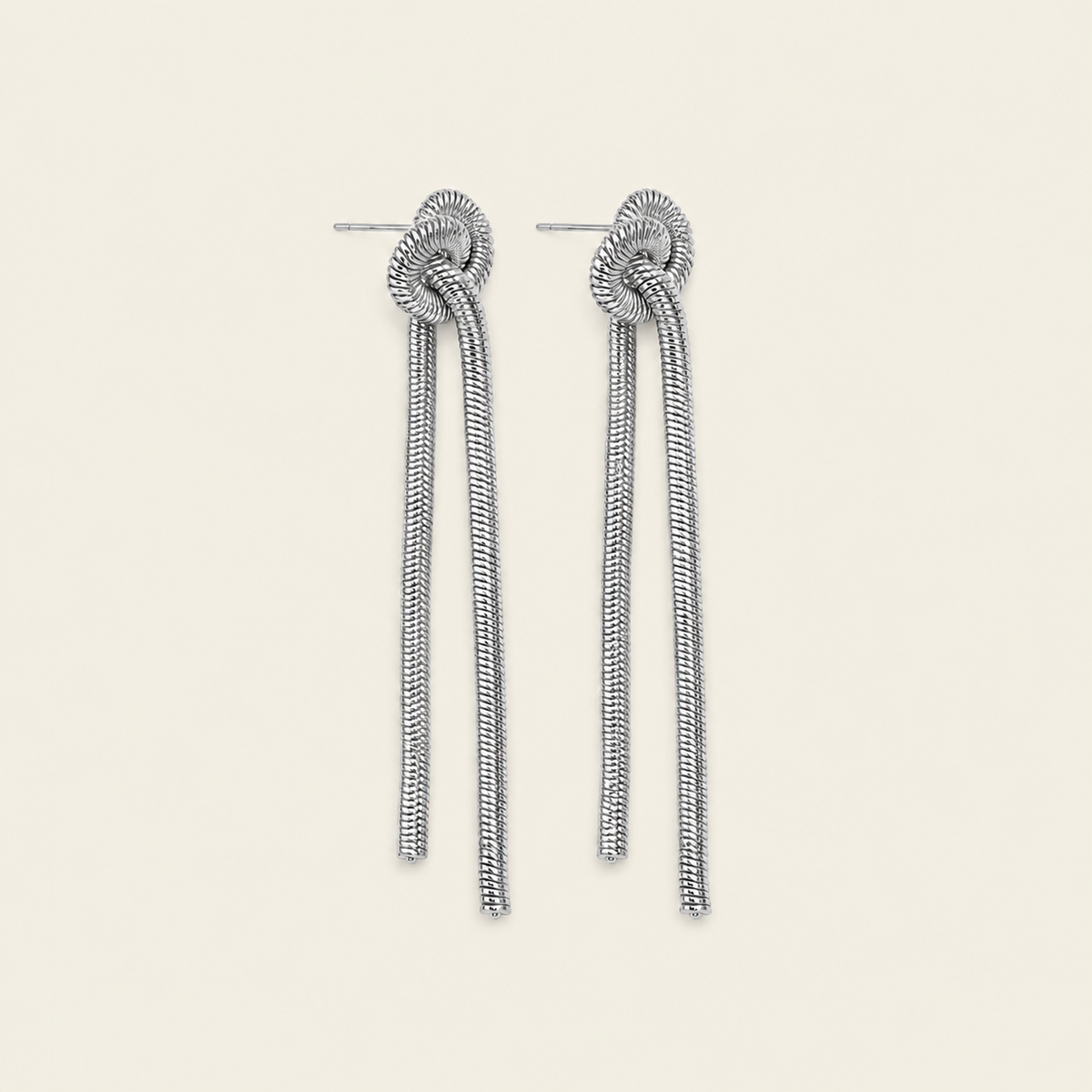 A pair of silver-toned drop earrings with a knotted spiral design at the top and long, textured snake-like strands hanging below, shown on a plain light beige background.