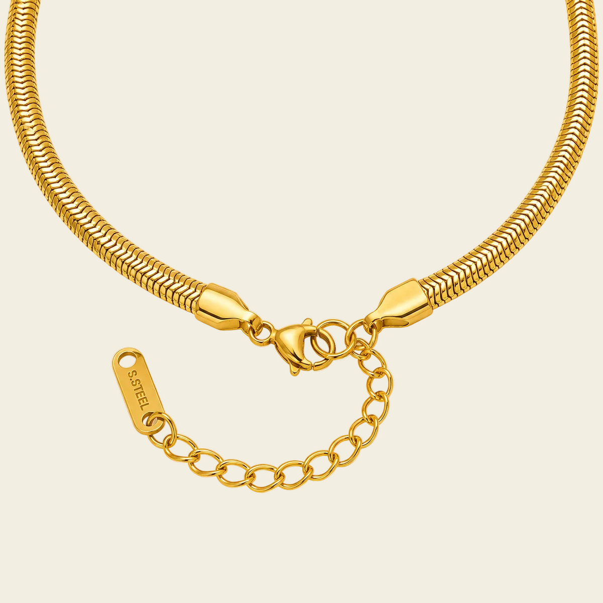 A close-up of a gold snake chain necklace with a lobster clasp, extender chain, and a branded tag engraved with 'SKELET'. The necklace is arranged in a U-shape against a solid pale peach background.