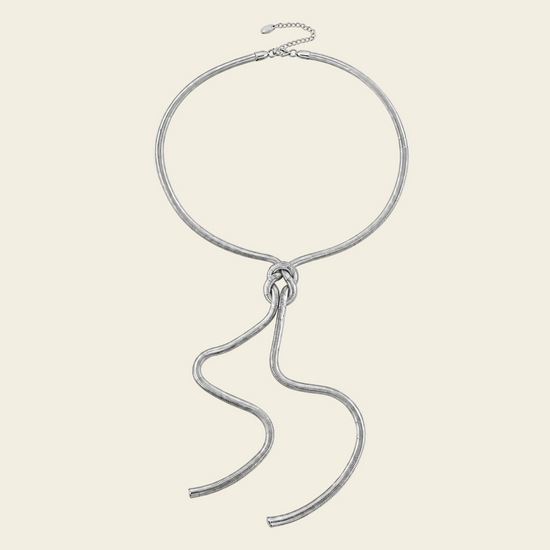 A textured silver-tone chain necklace with a large circular loop and a long, flowing snake-like drape, displayed on a solid cream background.