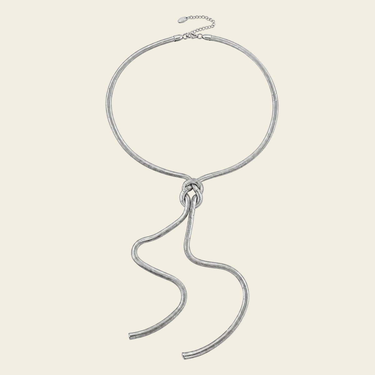 A textured silver-tone chain necklace with a large circular loop and a long, flowing snake-like drape, displayed on a solid cream background.