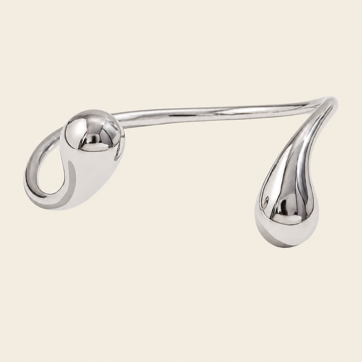 A polished silver-toned metal hair claw clip with a curved, sculptural design featuring a spherical loop on one end and a teardrop-shaped loop on the other, set against a solid light beige background.