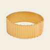 A wide gold bangle bracelet with a ribbed, fluted exterior and a smooth interior, shown on a light beige background.