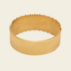 A wide, polished gold bangle bracelet with a textured, scalloped edge, shown on a light cream background.