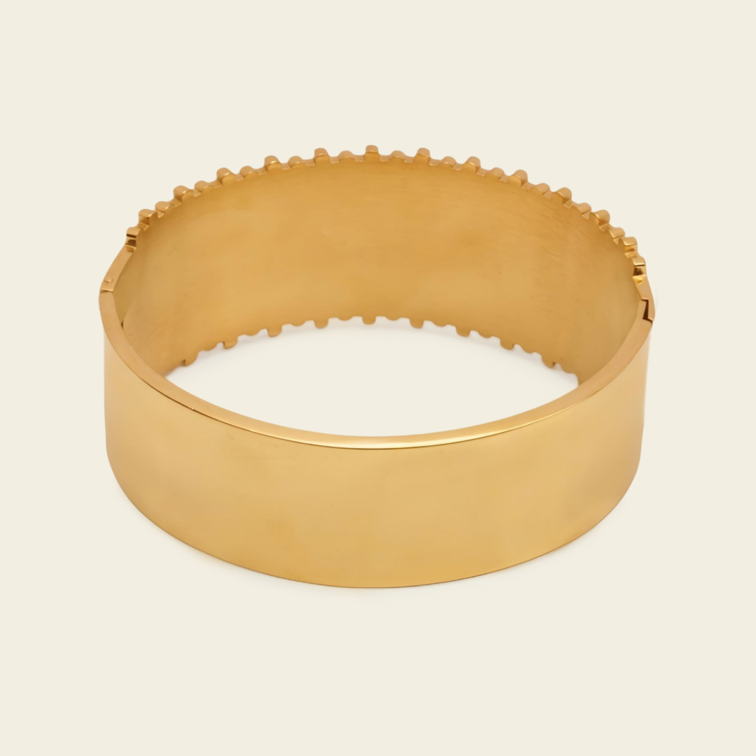 A wide, polished gold bangle bracelet with a textured, scalloped edge, shown on a light cream background.