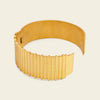 A wide gold-toned cuff bracelet with a ribbed, fluted exterior and a smooth inner band, shown on a plain light beige background.