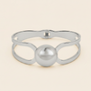 A polished silver-tone metal cuff bracelet with a central spherical bead and openwork loop details, shown on a light cream background.
