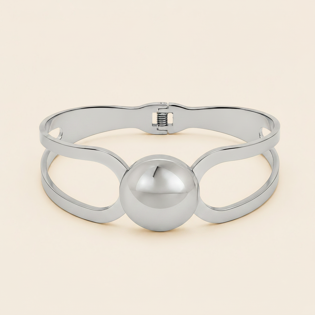 A polished silver-tone metal cuff bracelet with a central spherical bead and openwork loop details, shown on a light cream background.
