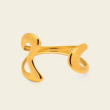 A polished gold open cuff ring with an abstract, flowing sculptural design, shown on a light cream background.
