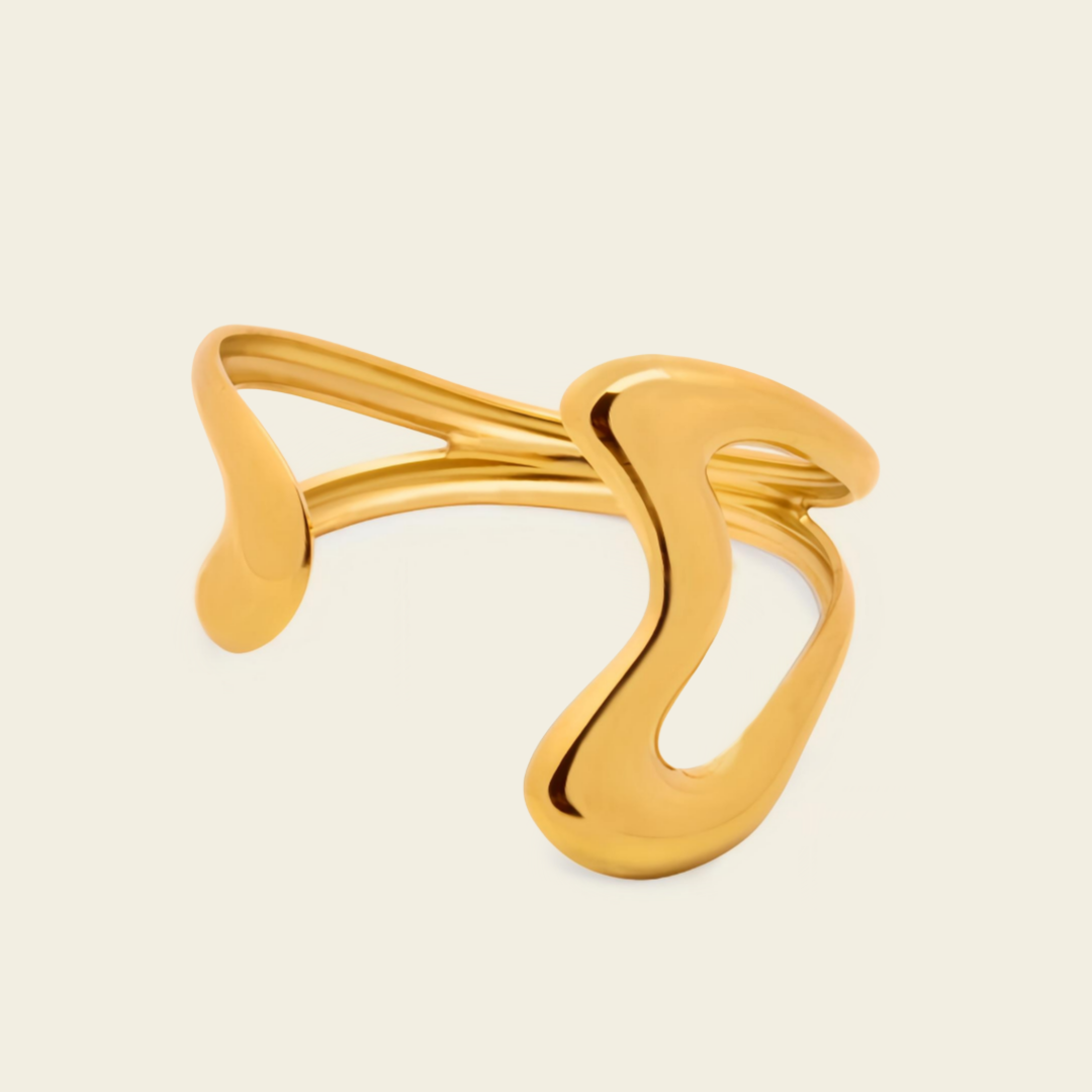 A polished gold abstract open cuff ring with a smooth, flowing organic design, shown on a light cream background.