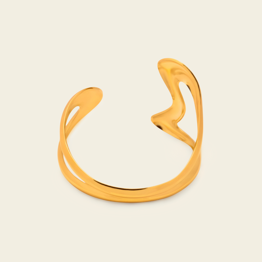 A polished gold-toned open cuff ring with a smooth, organic wavy design, displayed on a solid off-white background.