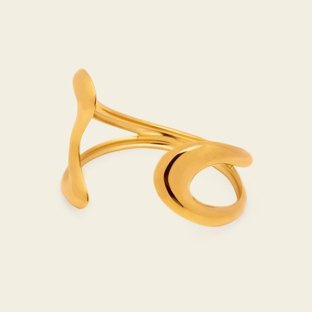 A polished gold abstract ring with a sculptural, flowing design, photographed on a clean, solid off-white background.