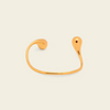 A minimalist gold open cuff bracelet with a curved, organic teardrop-shaped end, shown on a light cream background.