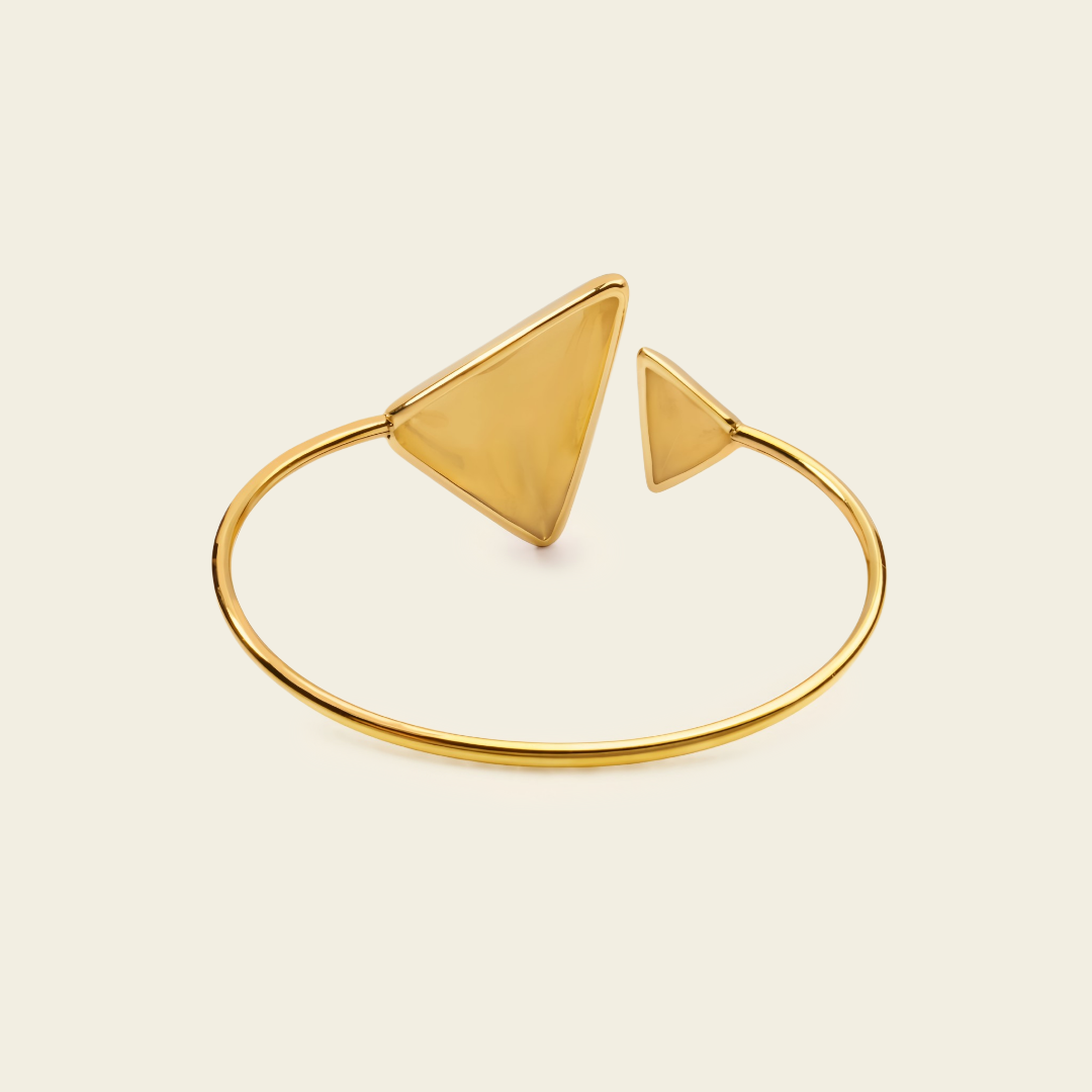 A gold-toned open bangle bracelet with two triangular geometric charms, displayed on a light cream background.