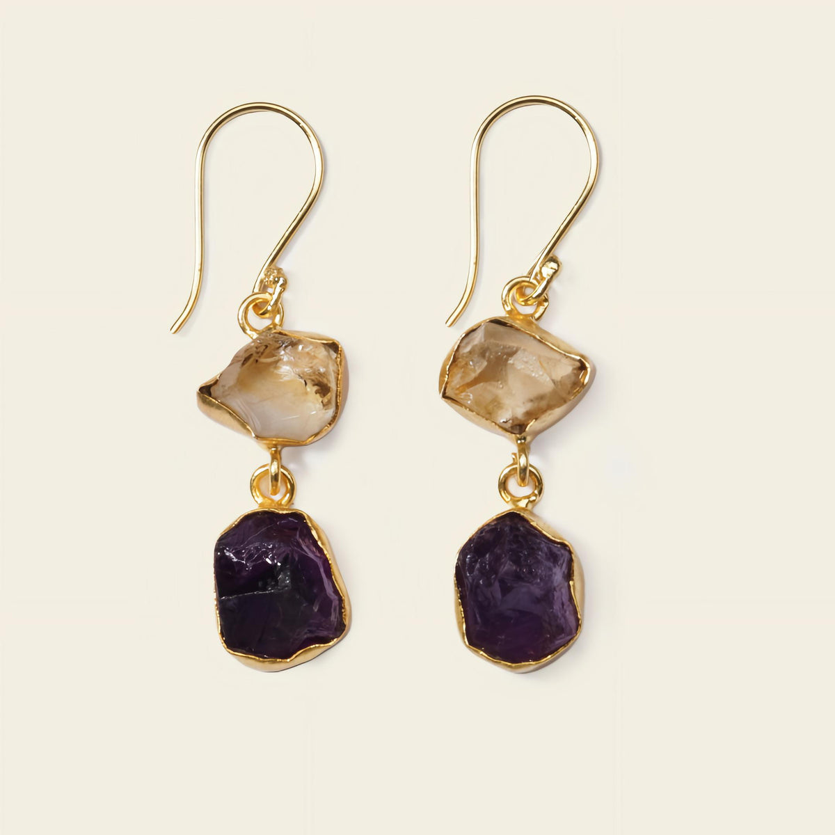 Gold earrings with purple and brown gemstones on a beige background