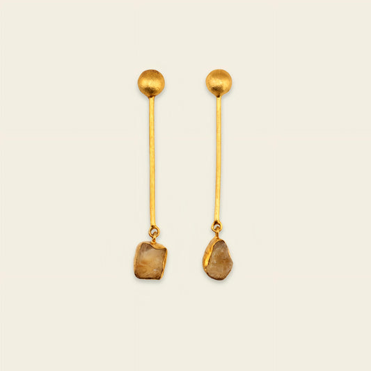 Pair of gold earrings with dangling stones on a beige background