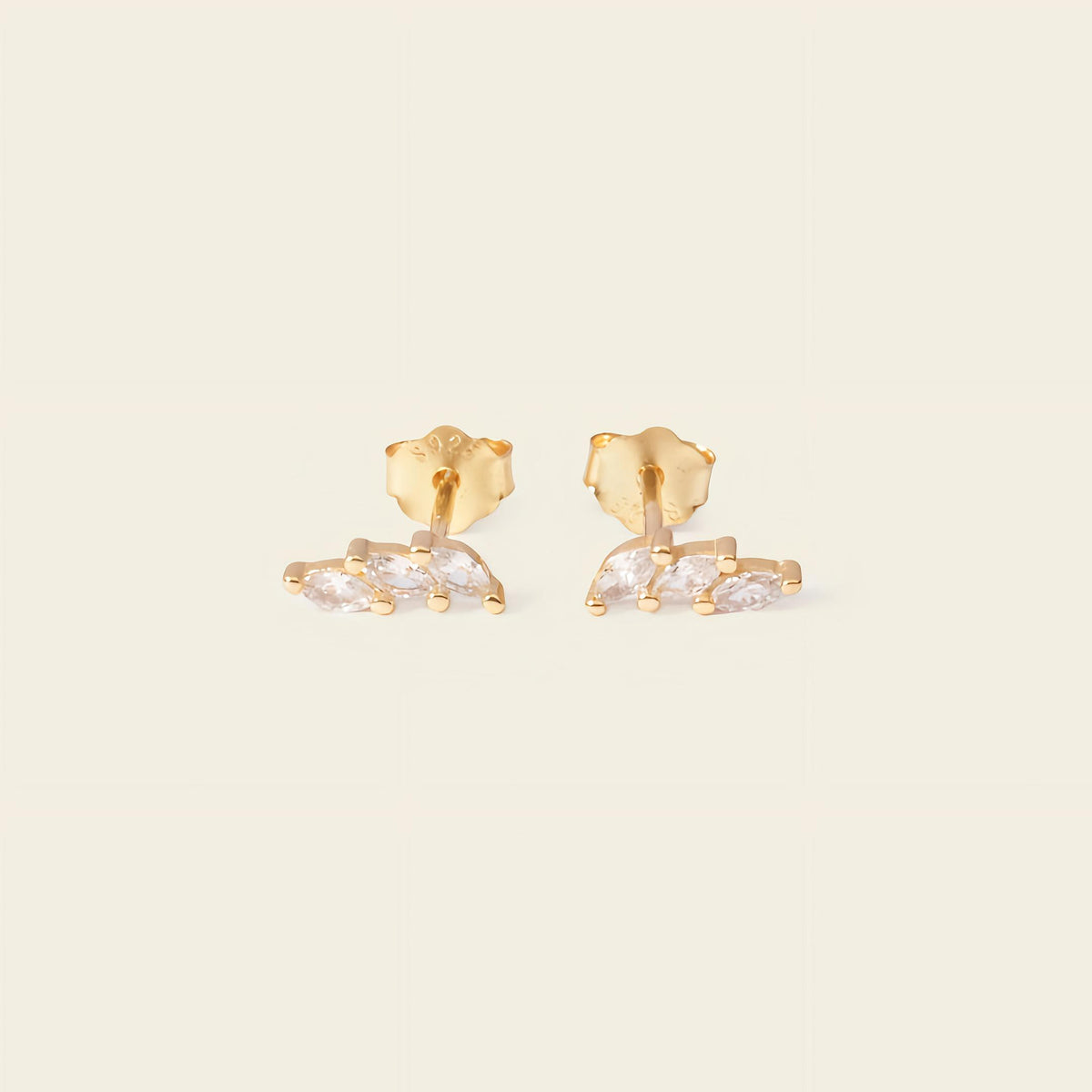Gold earrings with clear stones on a beige background