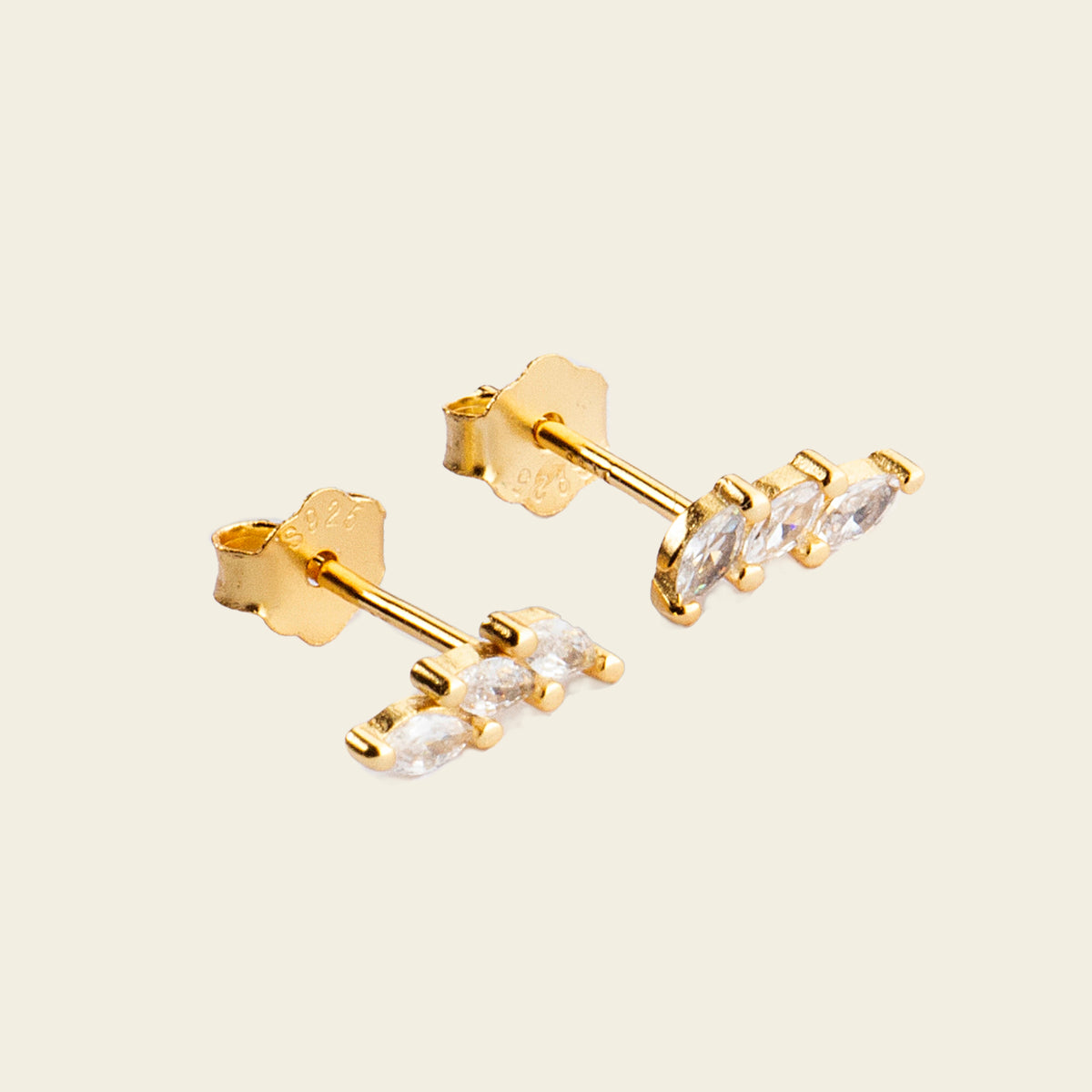 Gold earrings with clear gemstones on a beige background