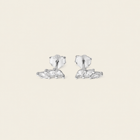 A pair of silver stud earrings with marquise-cut clear stones, displayed on a solid light beige background.