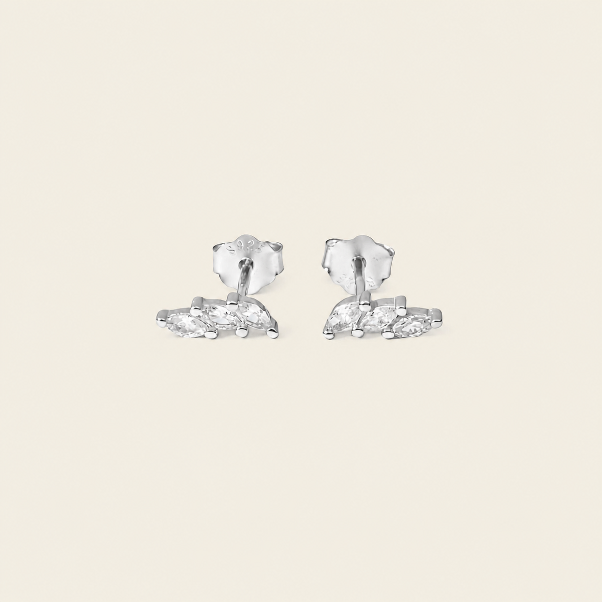 A pair of silver stud earrings with marquise-cut clear stones, displayed on a solid light beige background.