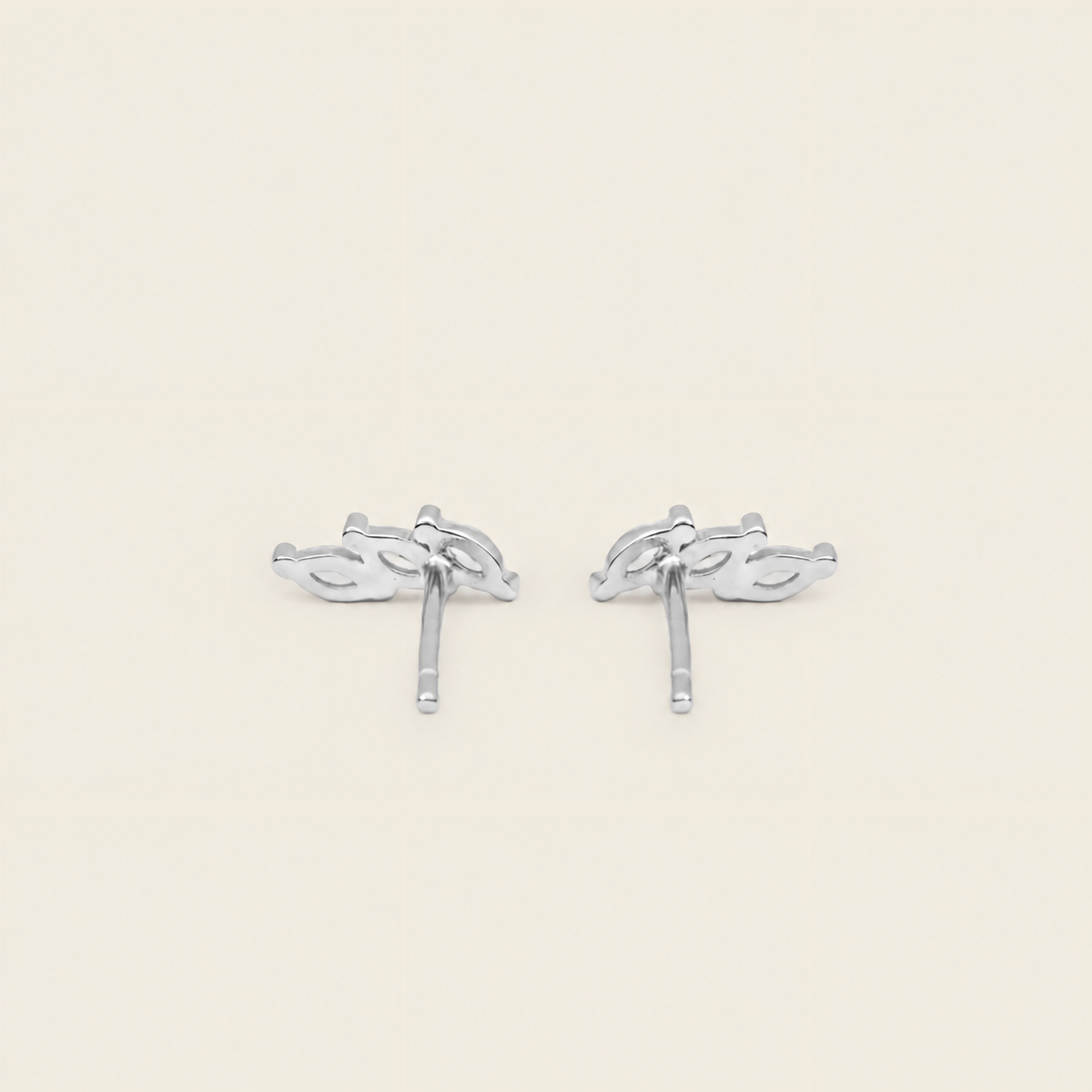 A pair of silver-toned stud earrings with a stylized leaf or vine motif, shown on a plain light beige background.