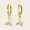 Gold hoop earrings with butterfly charms on a beige background