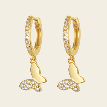 Gold hoop earrings with butterfly charms on a beige background