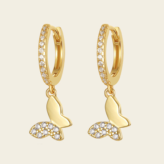 Gold hoop earrings with butterfly charms on a beige background