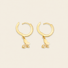 A pair of gold huggie hoop earrings with dangling butterfly charms, one butterfly in solid gold and the other encrusted with small clear stones, set against a light beige background.