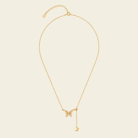 Gold necklace with a butterfly pendant on a beige background
