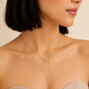 A close-up of a model wearing a delicate gold chain necklace with a butterfly pendant and a small dangling star, set against a soft beige background.