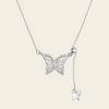 A silver butterfly pendant necklace with a delicate chain, a larger butterfly pendant encrusted with small clear stones, and a smaller dangling butterfly charm, shown on a solid light beige background.