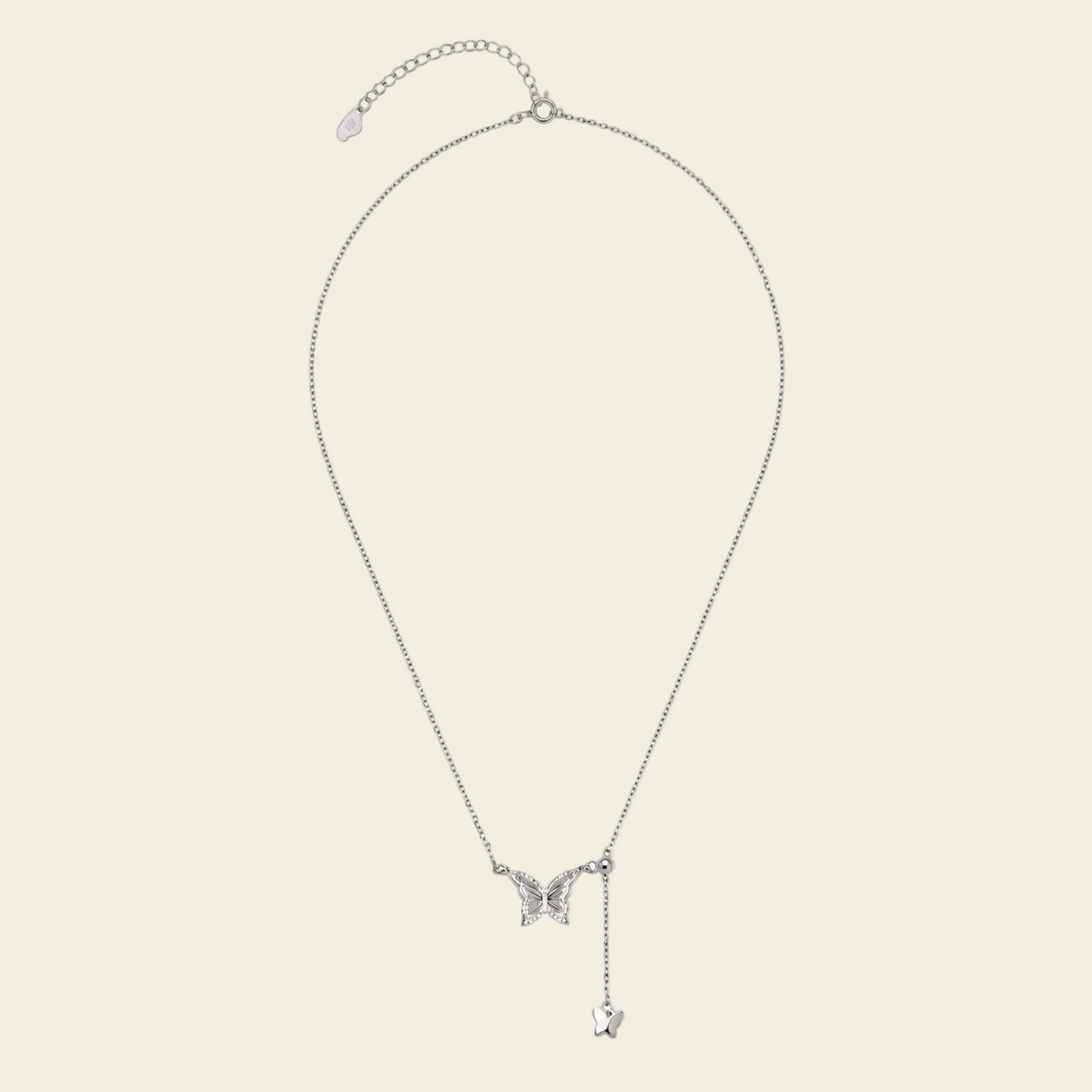 A delicate silver chain necklace featuring a small butterfly pendant and a dangling heart charm, displayed against a solid light beige background.