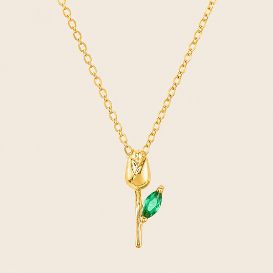 Gold necklace with a green gemstone pendant on a beige background.