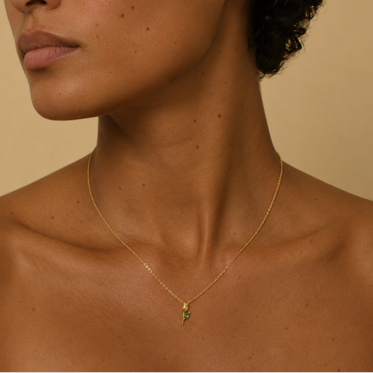 Woman wearing a gold necklace with a green pendant against a beige background