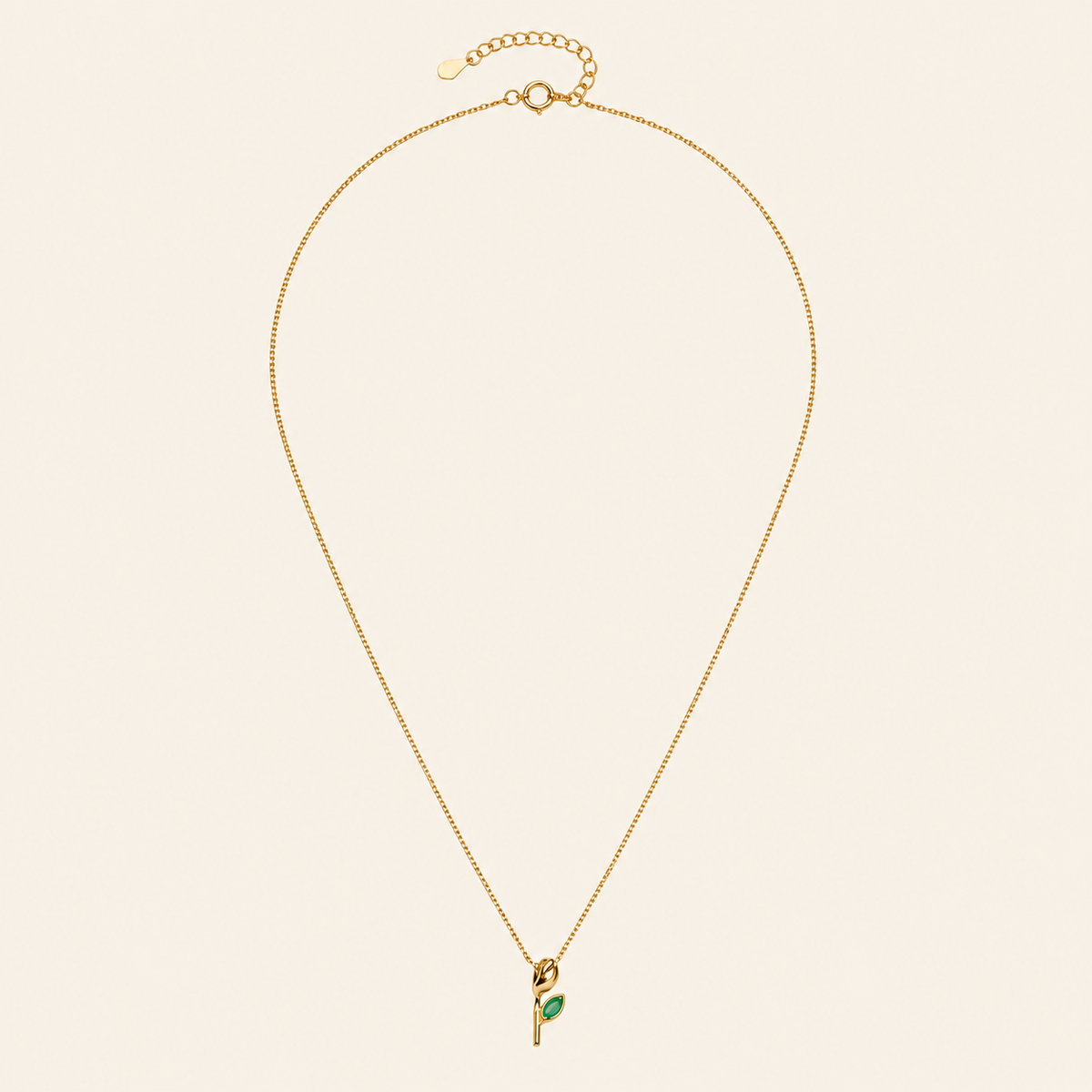 Gold necklace with a green pendant on a beige background