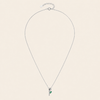 A delicate silver chain necklace with a small pendant featuring a green leaf detail, displayed on a solid light beige background.
