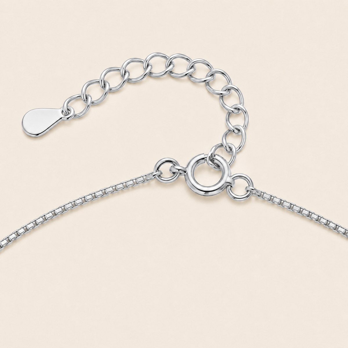 Close-up of a silver chain necklace showing the extender chain, clasp, and tag on a light beige background.