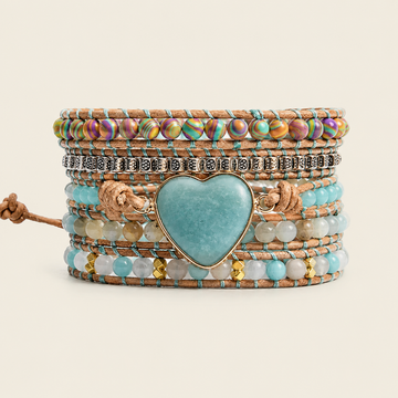 A stack of bohemian-style multi-layer bracelets featuring a large heart-shaped turquoise stone centerpiece, turquoise beads, iridescent beads, silver-toned metal charms, and brown cord wraps, set against a solid light beige background.