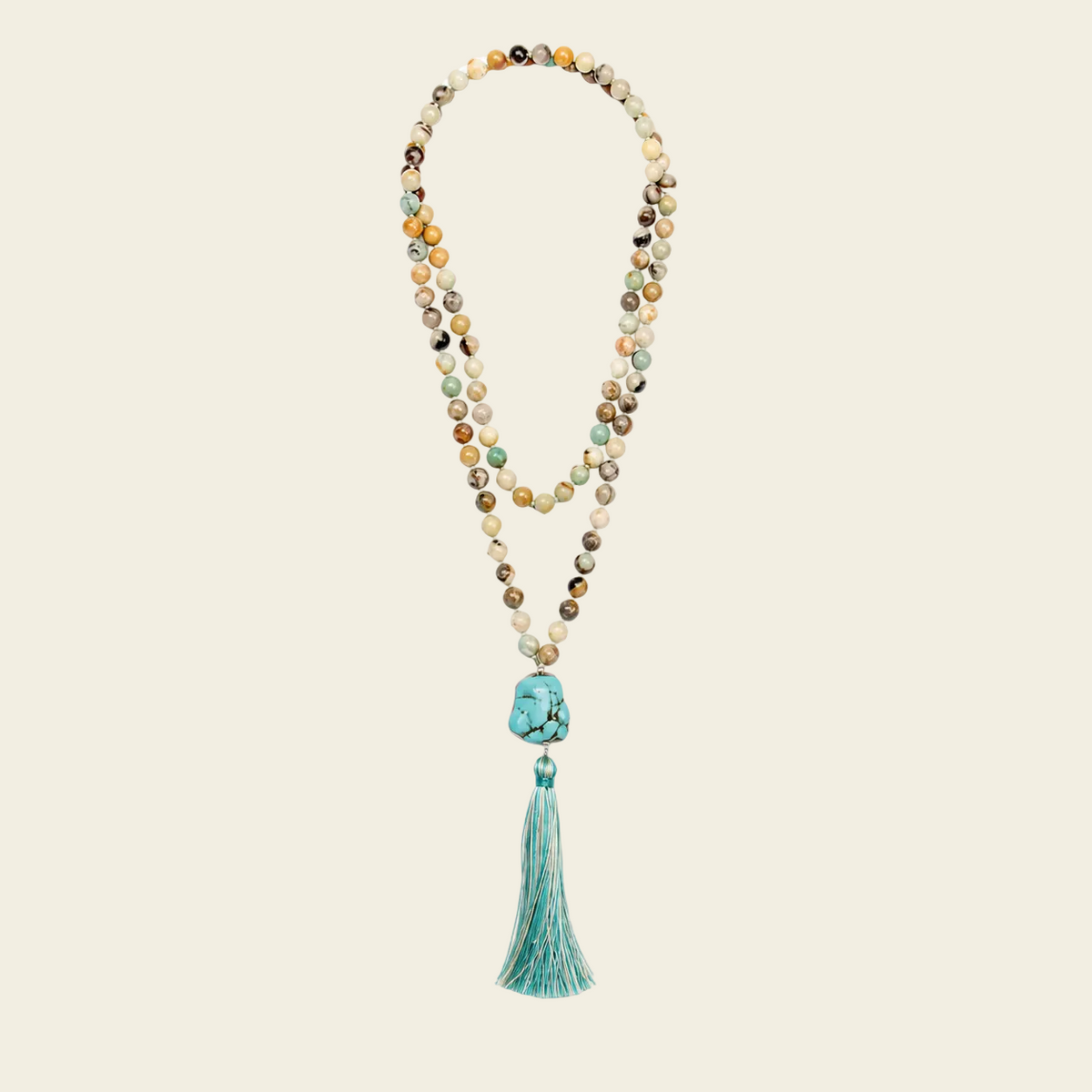 A multi-strand beaded necklace with a turquoise tassel, featuring various earthy and pastel beads with a prominent turquoise stone and tassel at the center, set against a solid pale beige background.