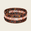 A stack of four copper wire bracelets wrapped with multi-strand beads in earthy brown, pink, white, and dark gray marbled stone, shown on a light beige background.