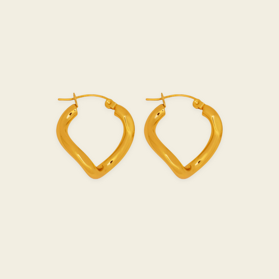 A pair of gold-toned, open hoop earrings with a textured, organic wavy shape, displayed on a solid light beige background.