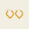 A pair of gold-toned, open hoop earrings with a textured, organic wavy shape, displayed on a solid light beige background.