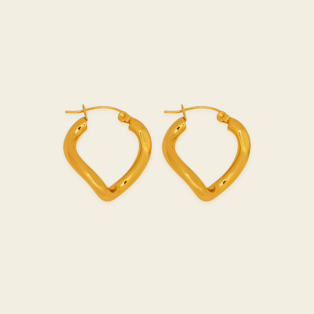 A pair of gold-toned, open hoop earrings with a textured, organic wavy shape, displayed on a solid light beige background.