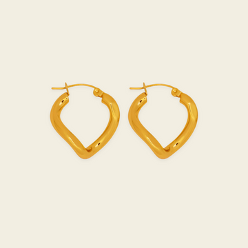 A pair of gold-toned, open hoop earrings with a textured, organic wavy shape, displayed on a solid light beige background.