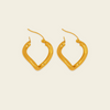 A pair of gold-toned, abstract open hoop earrings with curved, organic edges and fishhook backings, displayed on a solid, warm off-white background.