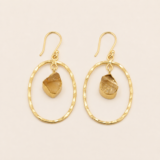 Gold hoop earrings with natural stone drops on a beige background