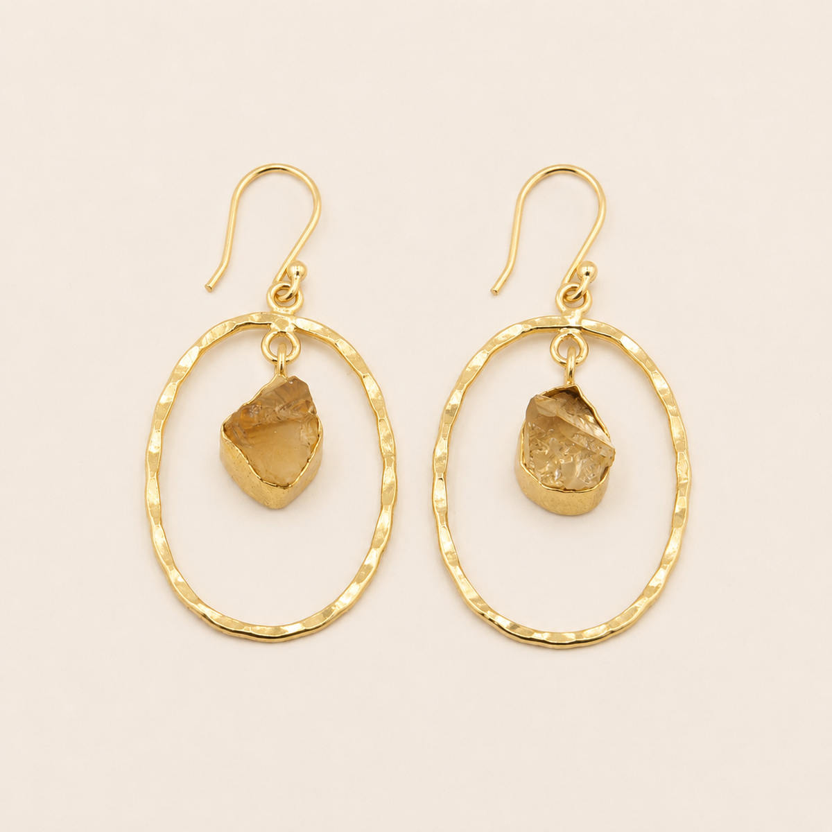 Gold hoop earrings with natural stone drops on a beige background